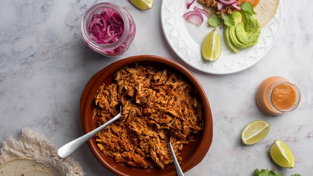 Mexican pollo pibil shredded in a bowl and served in a corn tortilla with pickled onions and habanero salsa.