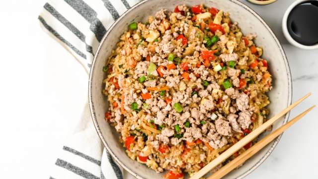 Pork fried cauliflower rice with ground pork, cauliflower rice, cabbage, carrots, and green onion in a bowl with chopsticks.