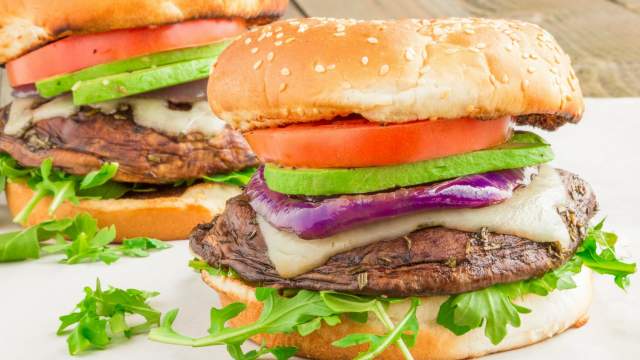 Portobello burgers with avocado, swiss cheese, tomatoes, and lettuce on a bun.