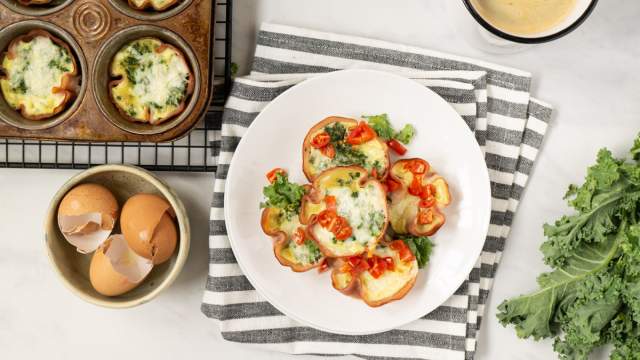 Quiche cupcakes with a ham crust and a cheese and spinach filling on a wire rack with cracked eggs on the side. 