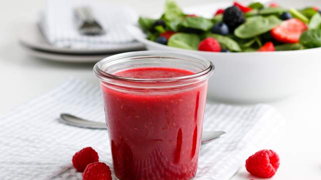 Raspberry vinaigrette dressing in a glass jar with raspberries and a green salad.