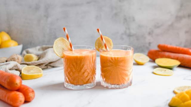 Carrot ginger smoothie with shredded carrots, banana, and mango in two glasses with straws.