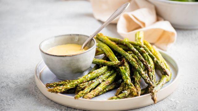 Roasted asparagus with olive oil, salt, and pepper served on a plate with hollandaise sauce.