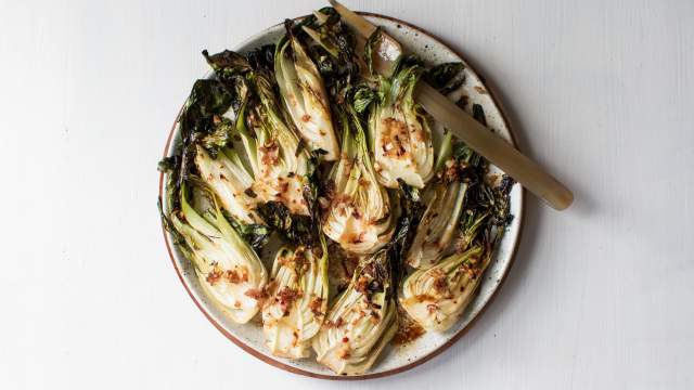 Roasted bok choy with soy sauce, garlic, ginger, and sesame seeds on a plate with a gold fork.