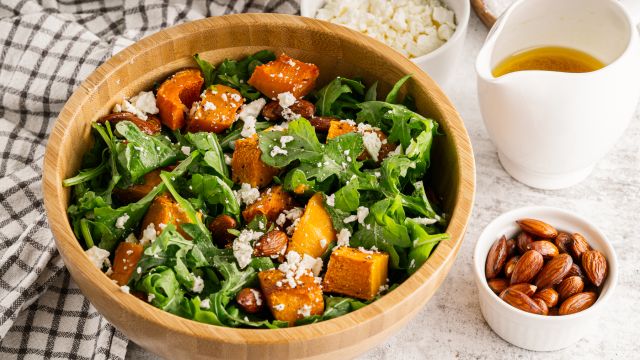 Roasted butternut squash salad with arugula, roasted squash, almonds, feta cheese, and orange vinaigrette in a wooden bowl.