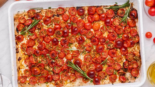 Roasted cherry tomatoes on a baking sheet with olive oil, rosemary, salt, and pepper.