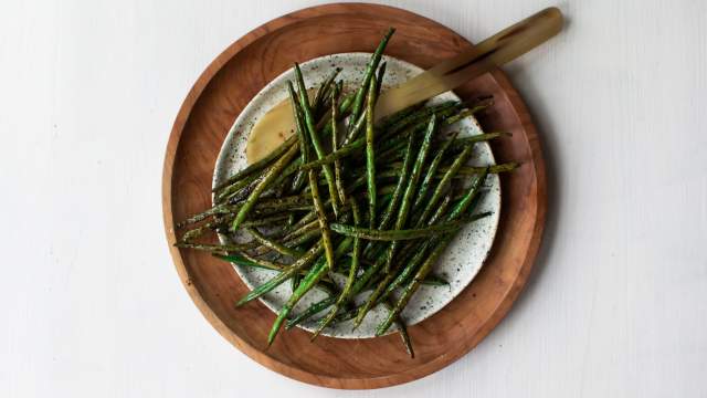 Roasted green beans with olive oil, balsamic vinegar, garlic powder, salt, pepper, and Italian seasoning on a wooden plate with a spoon. 