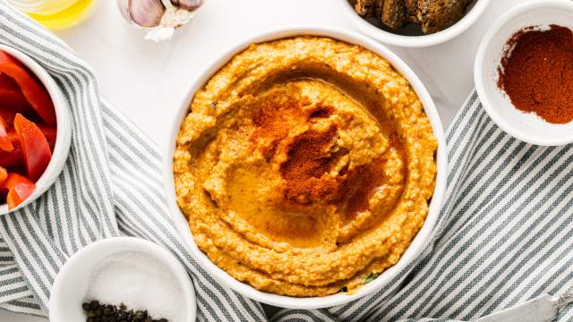 Roasted red pepper dip in a bowl drizzled with olive oil with garlic, crackers, and red bell pepeprs on the side.