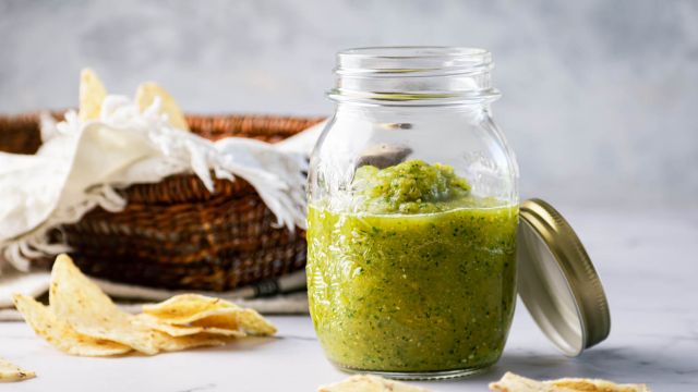 Roasted salsa verde with tomatillos, jalapenos, and cilantro in a mason jar with chips on the side.