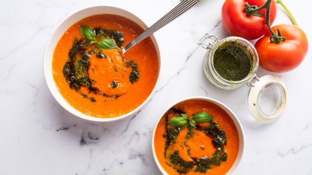 Roasted tomato basil soup in two bowls with pesto and fresh basil leaves.