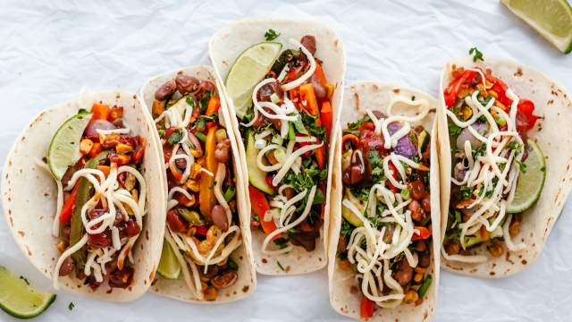 Roasted vegetable fajitas with bell peppers, onions, corn, carrots, zucchini, and pinto beans in tortillas with cheese and limes.