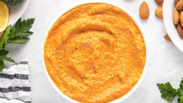 Romesco sauce with blended almonds, tomatoes, and red peppers in a small white bowl with parsley and lemon on the side.