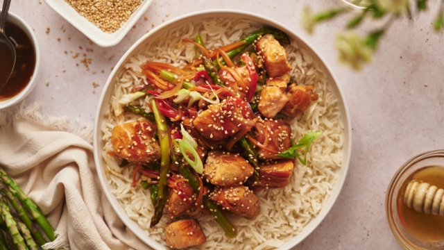 Salmon stir fry with chunks of salmon, asparagus, carrots, and red pepper in a bowl with steamed rice. 