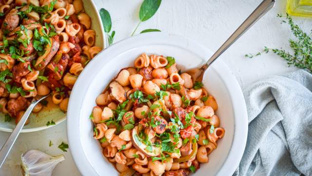 Sausage and pepper pasta with turkey sausage, bell peppers, onions, mushrooms, and tomato sauce in two bowls with garlic.