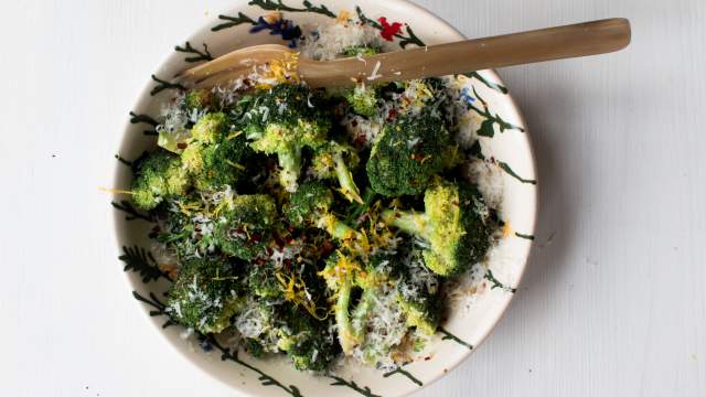 Sauteed broccoli with Parmesan cheese, lemon zest, red pepper flakes, and olive oil in a ceramic bowl with a wooden spoon.