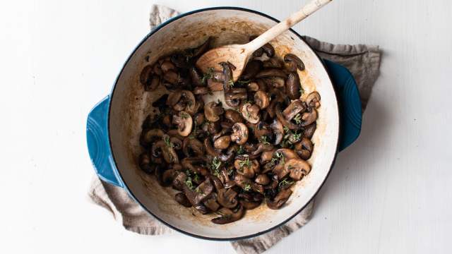 Sauteed mushrooms with garlic, butter, and thyme in a blue ceramic skillet.