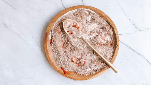 Homemade seasoned salt on a wooden plate with paprika, kosher salt, garlic powder, onion powder, and pepper.