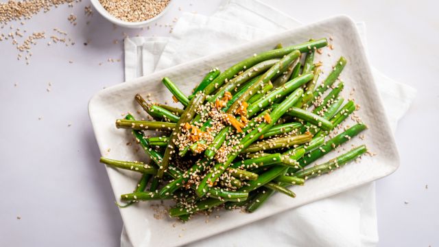 Sesame green beans on a plate with sautéed garlic, sesame seeds, and soy sauce.