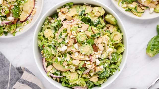 Shaved Brussels sprouts salad with creamy honey dijon dressing, sliced apples, goat cheese, almonds, and red onions in a bowl.