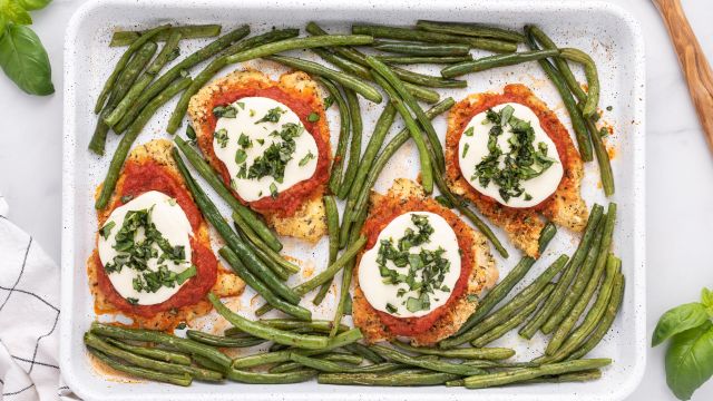 Healthy Chicken Parmesan with breaded chicken covered in sauce and cheese on a sheet pan with roasted green beans.