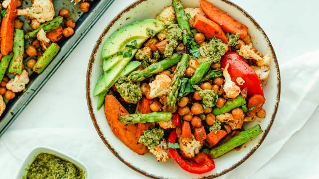 Sheet pan pesto chickpeas and vegetables on a plate with asparagus, sweet potatoes, chickpeas, carrots, cauliflower, and peppers.