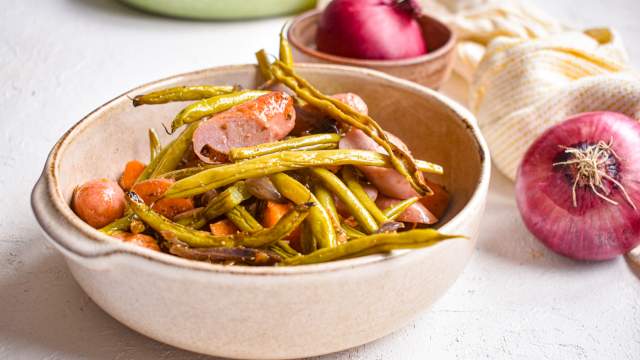 Sheet pan sausages, sweet potatoes, green beans, and red onions in a bowl with spices.