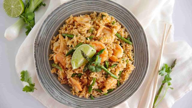 Shrimp fried rice with asparagus, cilantro, and a lime wedge in a bowl.