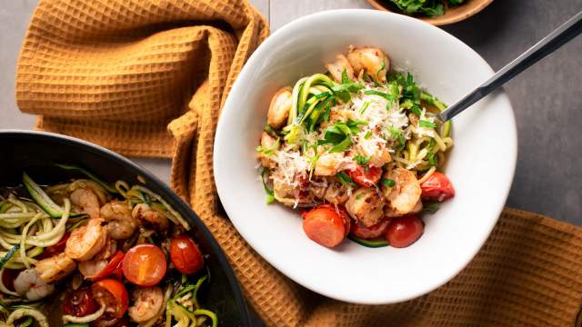 Healthy shrimp scampi zoodles with garlicky shrimp, tomatoes, Parmesan cheese, zucchini noodles, and parsley in a bowl.