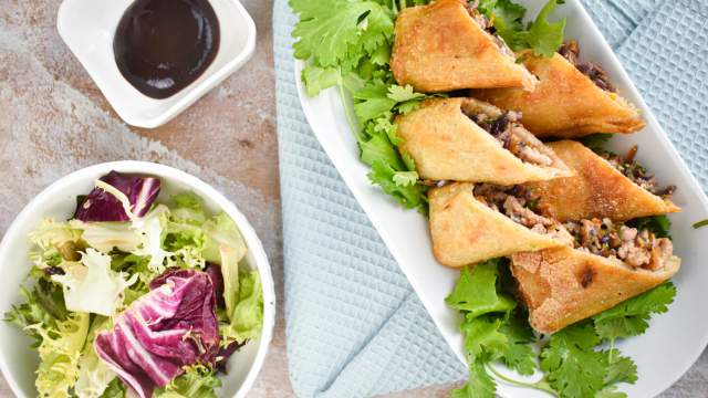 Baked egg rolls with cabbage, carrots, and ground chicken cut in half on a plate with oyster sauce.