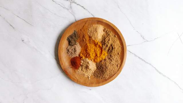 Homemade curry powder on a wooden plate with a variety of ground spices including cumin, coriander, cardamom, ginger, cinnamon, and cayenne.