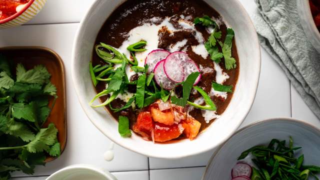 Slow cooker Black Bean Soup in a bowl with sour cream, cilantro, tomatoes, and radishes.