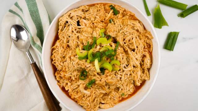 Slow cooker buffalo chicken shredded in a bowl with diced celery and buffalo sauce.