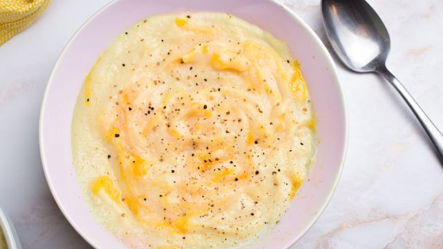 Slow cooker cheesy cauliflower soup with a metal spoon, shredded cheese, and black pepper.