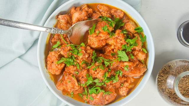 Slow cooker chicken and cauliflower tikka masala in a bowl with cilantro and spices on he side.