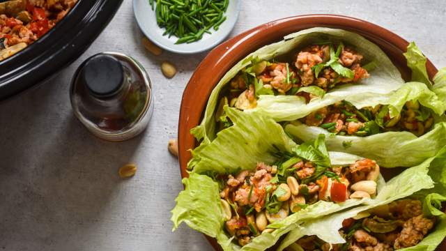 Slow cooker chicken lettuce wraps on a plate with lettuce leaves stuffed with chicken, mushrooms, peppers, and cilantro.