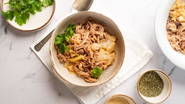 Slow cooker kalua pork with cabbage cooked with Hawaiian sea salt and liquid smoke in a bowl with cilantro on the side.