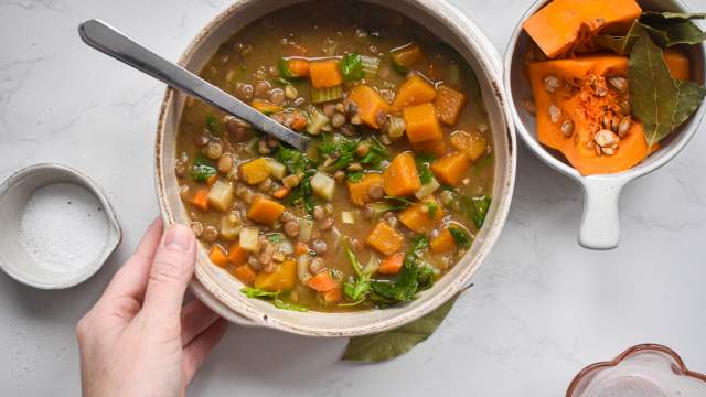 Slow cooker lentil soup with lentils, squash, carrots, spinach, and potatoes in a bowl with a hand holding it.