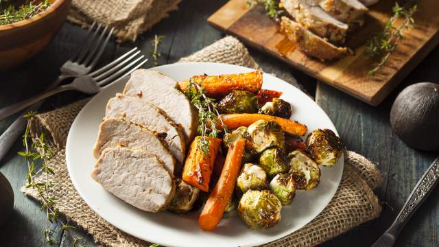 Slow Cooker Maple Pork Tenderloin sliced on a plate with carrots and Brussels sprouts.