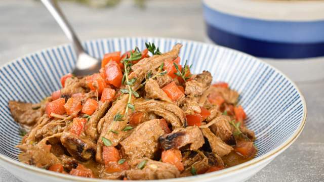 Slow cooker pork paprikash in a bowl with tomatoes and sour cream in a bowl.