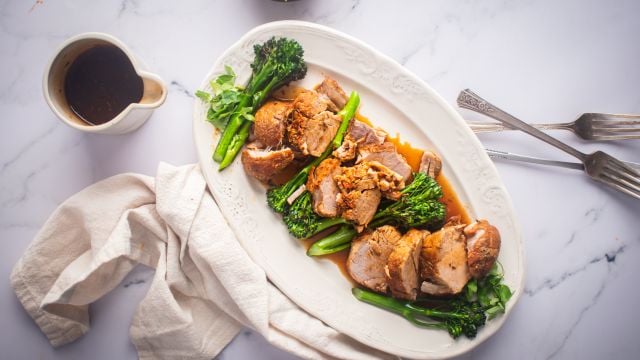 Slow cooker pork tenderloin with mustard sauce and broccolini on a white platter.