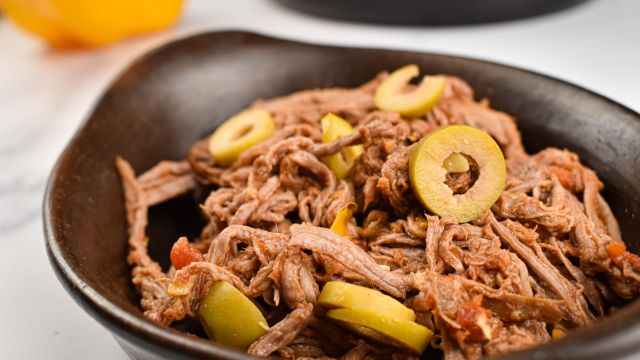 Slow cooker ropa vieja with peppers, onions, tomatoes, and olives in a black dish.