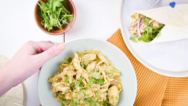 Slow Cooker Salsa Verde Chicken with shredded chicken, onions, and cilantro on a plate with tortillas.