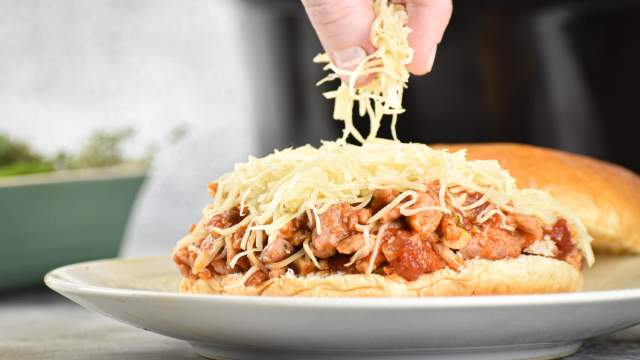 Slow cooker Tuscan turkey sloppy joes on a roll with shredded cheese.