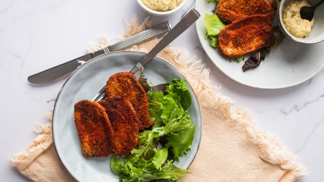 Spice crusted pork chops on a plate with mustard sauce and salad greens.