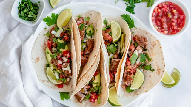 Steak tacos on flour tortillas with cilantro, onion, salsa, and lime.