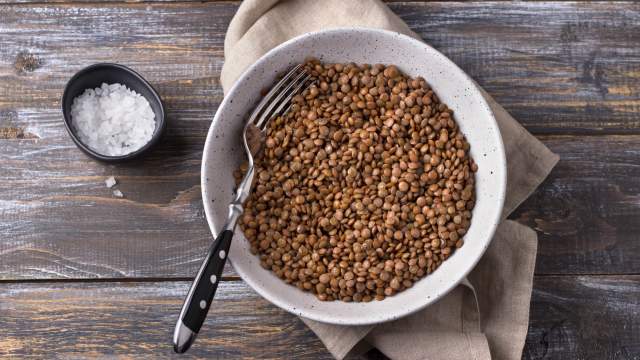 Cooked brown lentils in a white bowl with a napkin and fork.