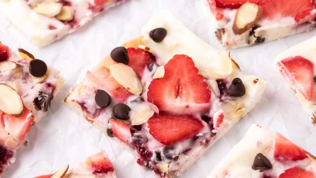 Strawberry frozen yogurt bark with chocolate chips, sliced almonds, and raspberry jelly broken into squares.