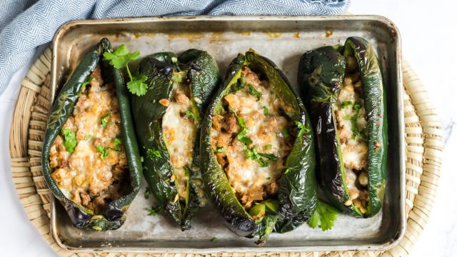 Stuffed poblano peppers with ground turkey, melted cheese, and mozzarella on a baking sheet.