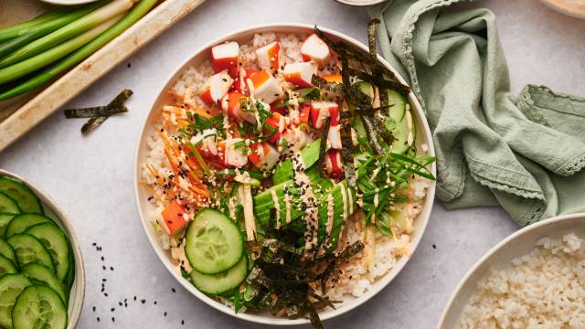 Sushi bowl with imitation crab, sushi rice, nori seaweed strips, cucumbers, carrots, and spicy mayo in a white bowl.