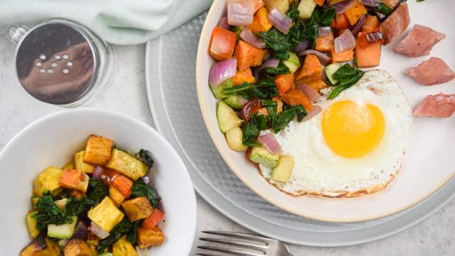 Sweet potato hash with sweet potatoes, zucchini, onions, peppers, and a fried egg on a plate with sliced sausage.